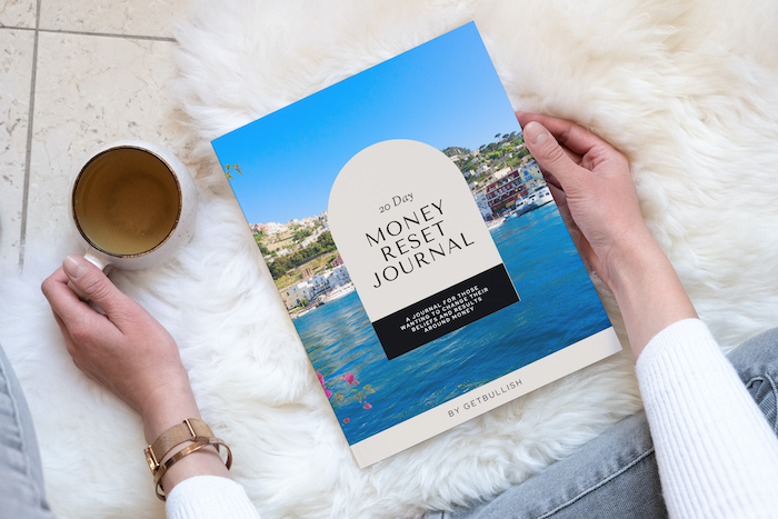 Woman's hands holding coffee and the GetBullish Money Reset book on a cozy blanket